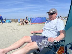 a-man-sitting-on-a-deck-chair-on-a-beach-who-looks-cold